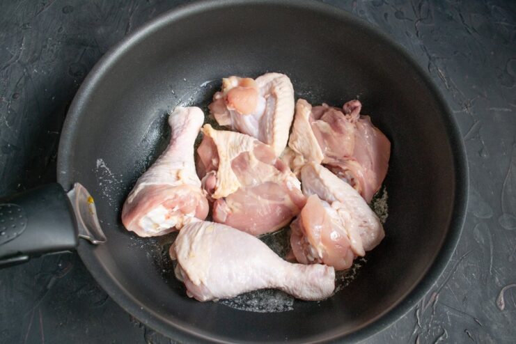 Chicken pieces being seared on one side in a hot skillet with melted butter.