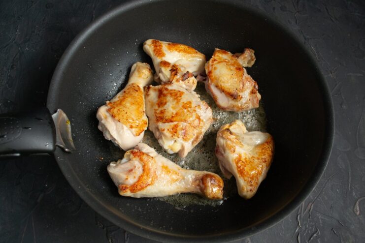 Flipping the chicken pieces in the skillet to brown them on the other side.