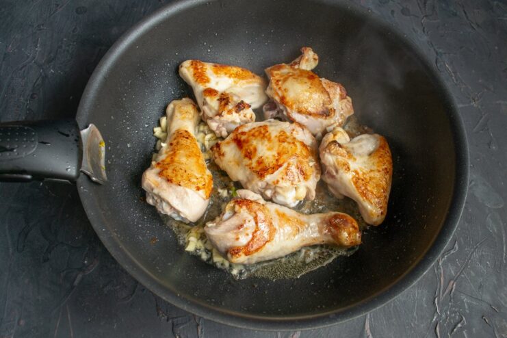 Minced garlic being added to the skillet with the seared chicken.