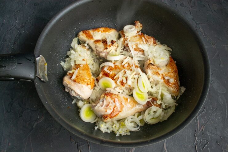 Chopped onions and leeks being added to the chicken in the skillet.