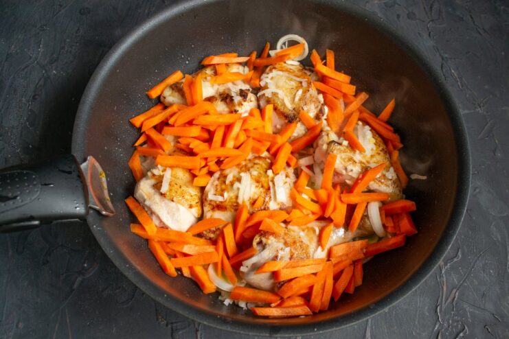 Carrot batons being added to the skillet with chicken and onions.
