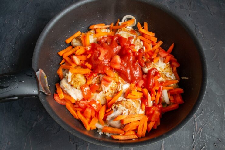 Adding a spoonful of tomato paste to the chicken and vegetables in the skillet.