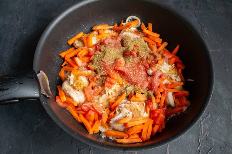 Spices, including paprika and khmeli-suneli, being sprinkled into the skillet.