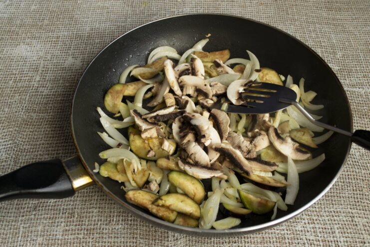 Cooking the mushrooms to release their earthy flavor Sliced mushrooms being added to the pan with vegetables and simmered.