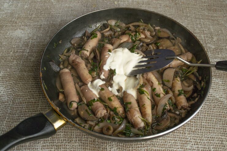 Finishing the sauce with heavy cream for a creamy texture Heavy cream being poured into the pan, and sausages being sliced with kitchen shears.