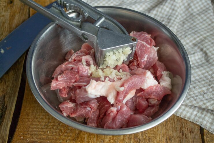 A bowl with sliced raw meat and minced garlic being added for the marinade.