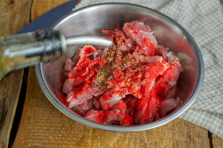 Meat in a bowl being seasoned with spices and olive oil before marinating.
