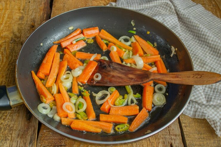 Chopped carrots, green onions, and chili being sautéed in a skillet.