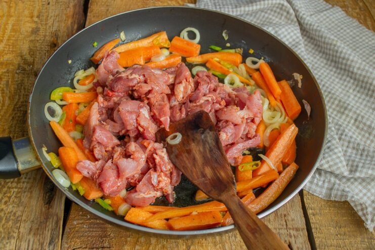 Sautéed vegetables pushed to one side of a skillet, with marinated meat added to the center.