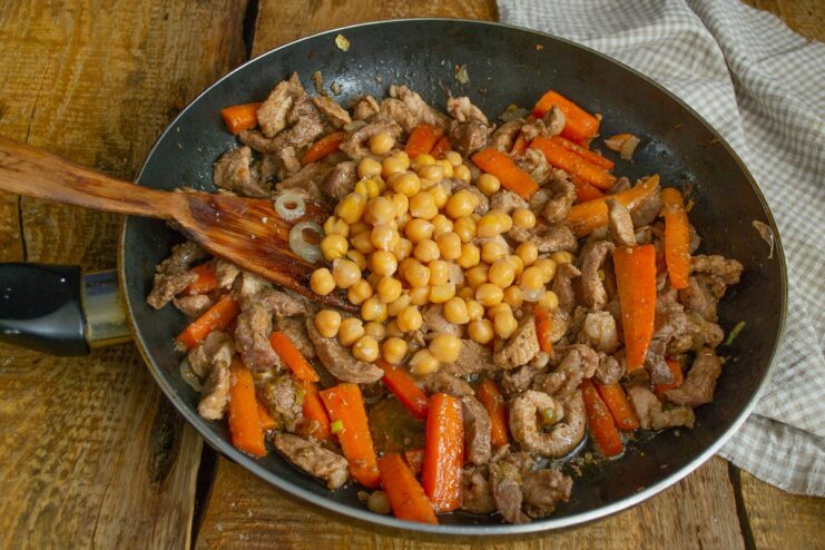 Cooked chickpeas being added to the skillet with meat and vegetables.