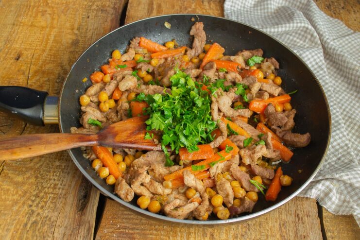 Fresh cilantro being added to the chickpea and meat mixture in the skillet before simmering.