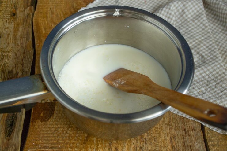 Whisking hot cream into a roux in a saucepan to create a smooth sauce.
