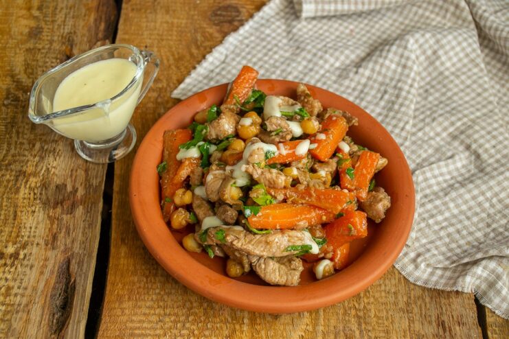 A finished plate of chickpeas and meat generously topped with creamy cheese sauce, ready to serve.