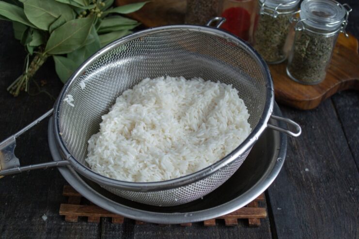 Rinsing Rice Until Water Runs Clear for Fluffy Plov White long-grain rice in a sieve being rinsed under running water.