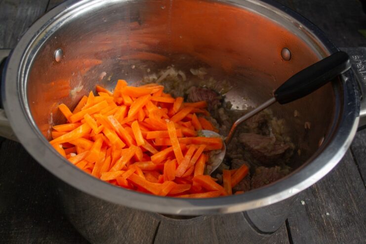 Adding Carrots to the Beef and Onions Carrot sticks being added to the pot with frying beef and onions.