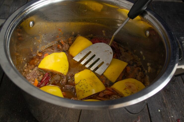 Layering Quince Over the Meat Base Slices of quince being layered over the meat and vegetable mixture in the pot.