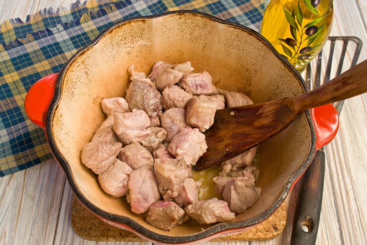 Cubes of meat being seared in a cast-iron pot until golden brown.