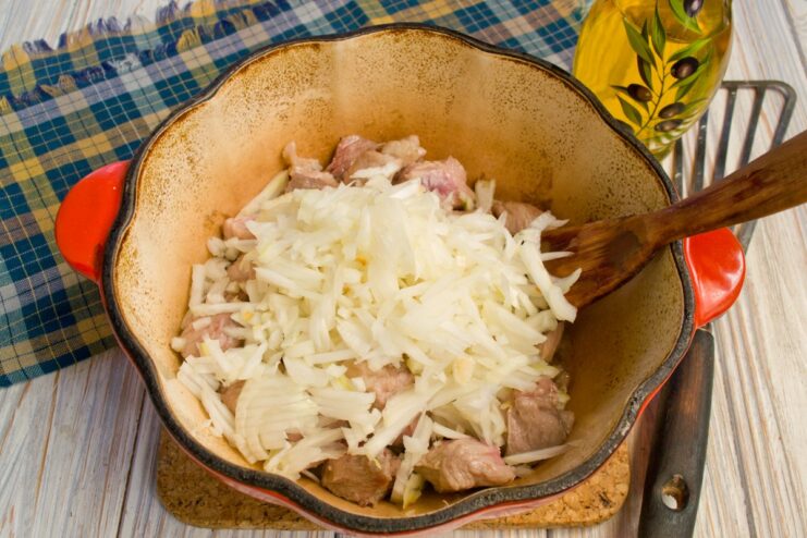 Chopped onions being added to the seared meat in the pot.