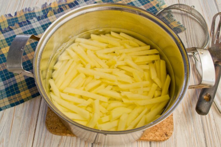 Peeled potatoes being cut into large strips on a cutting board.