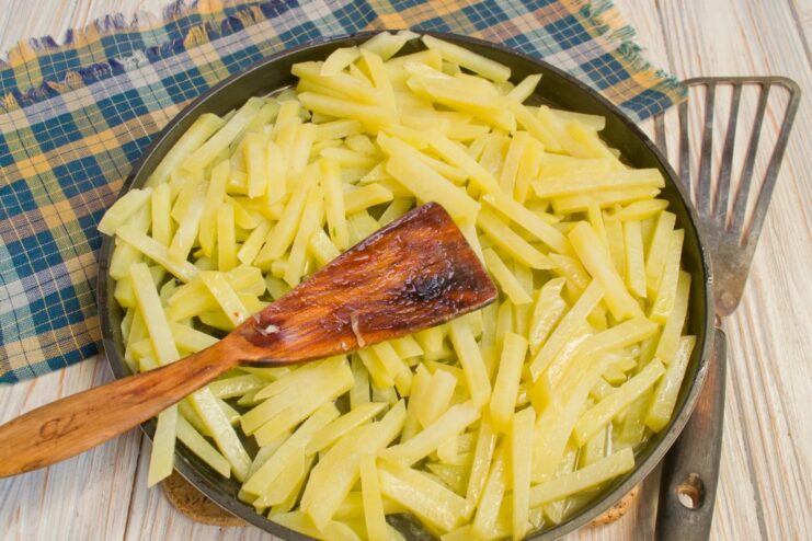 Potato strips being fried in a skillet until golden and crispy.