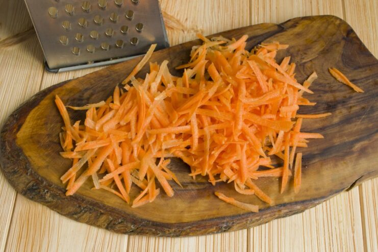 Adding Grated Carrots to the Sautéed Onions Grated carrots and chopped onions being fried together in a pan.