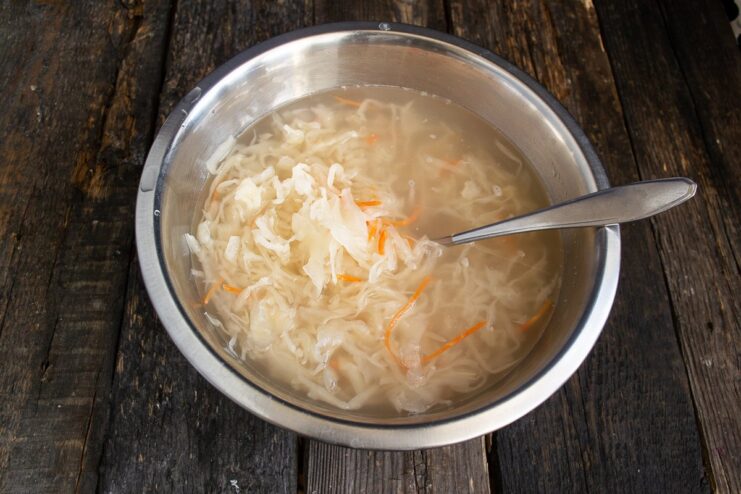 Rinsing sauerkraut to remove excess sourness before cooking Bigos. Sauerkraut in a colander being rinsed under running water.