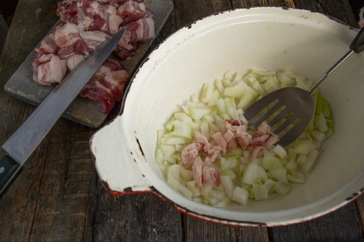 Rendering pork fat and sautéing onions to build the flavor base for Bigos. Diced pork fat and onions being sautéed in a Dutch oven.