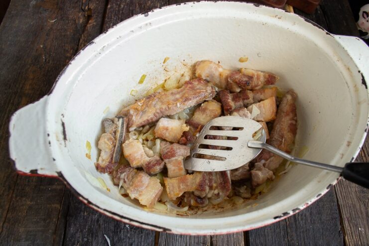 Searing pork belly chunks until golden brown for a richer stew. Chunks of pork belly being seared in a Dutch oven with onions.