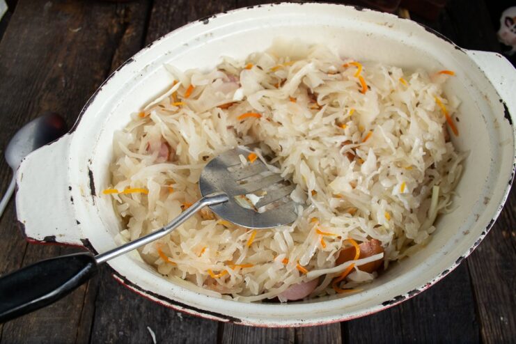 Topping the Bigos with a final layer of sauerkraut before stewing. A layer of sauerkraut covering the meat and fresh cabbage in the Dutch oven.