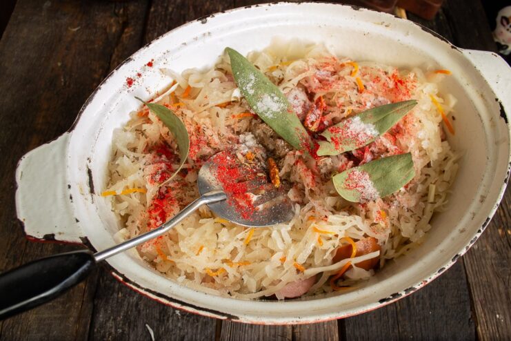 Adding white wine and spices like paprika and caraway to the stew. Dry white wine and spices being added to the pot with all the Bigos ingredients.
