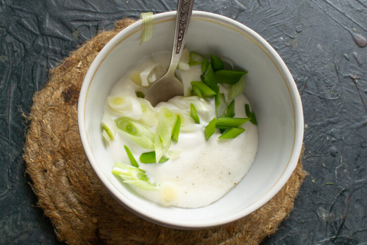 Preparing the creamy Greek yogurt and green onion sauce. A small bowl with Greek yogurt and chopped green onions being mixed for a sauce.