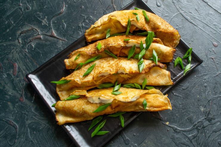 Serving the savory crepes with a dollop of yogurt sauce. A serving of rolled crepes with cheese on a plate, with a side of yogurt sauce.