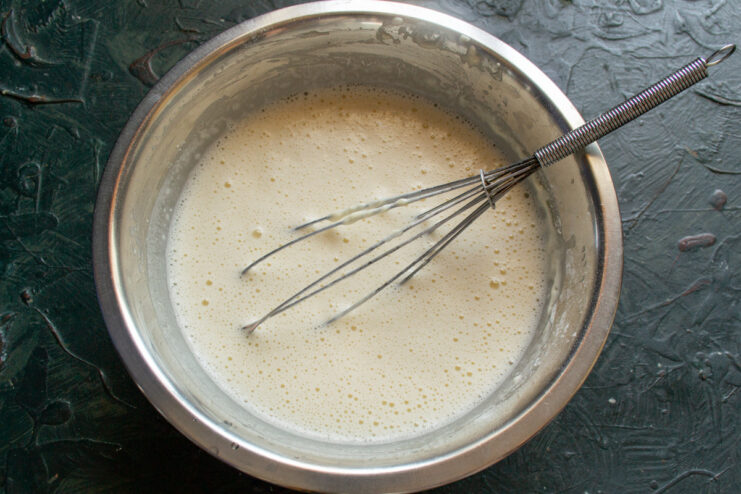 Letting the crepe batter rest is a key step for perfect texture. A bowl of crepe batter with a whisk in it, resting on a kitchen counter.