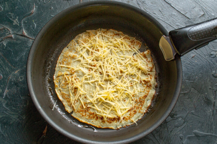 Grating hard cheese for the savory crepe filling. A block of hard cheese being grated on a box grater.