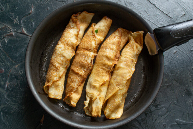 A useful tip: Keep your finished crepes warm in a buttered pan. Several rolled, filled crepes arranged in a large pan to keep warm.