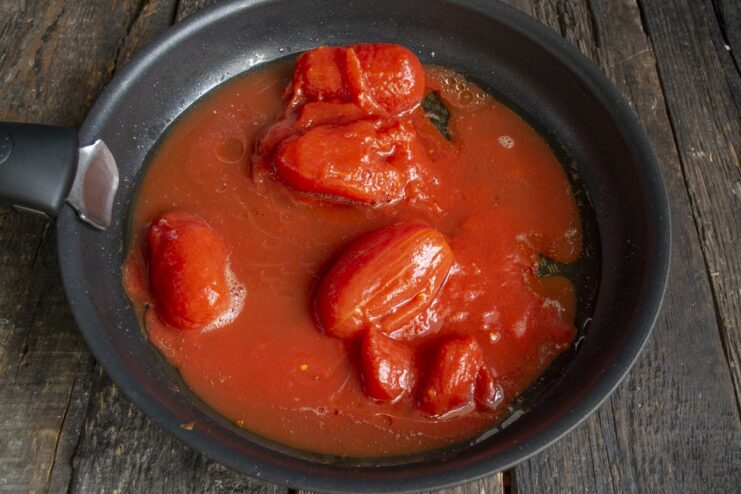 Making a Simple and Quick Tomato Sauce from Canned Tomatoes Canned tomatoes being mashed with a fork in a skillet to create a simple sauce.