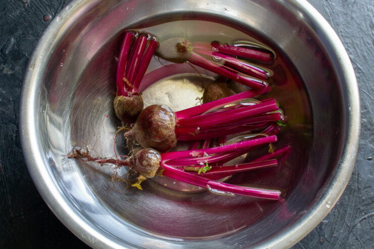 Young beets with their stems being washed in a bowl of cold water.
