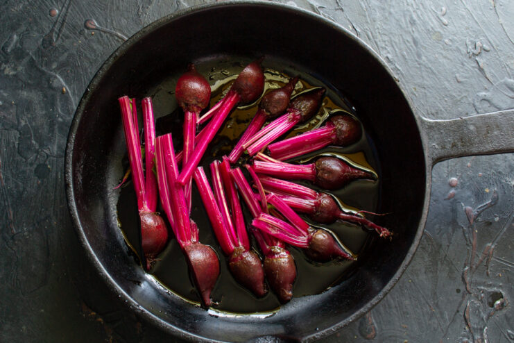 Halved young beets in a frying pan with oil, ready to be cooked.