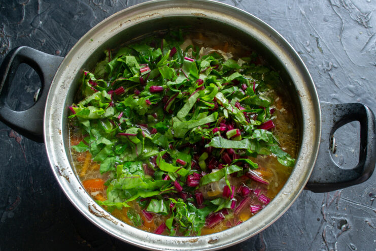 Fresh beet greens being shredded into thin strips on a cutting board.