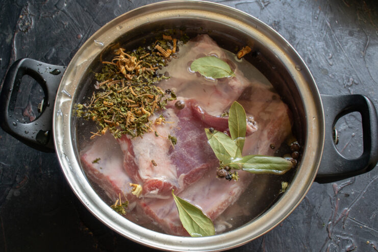 Raw pork ribs, root vegetables, and spices in a pot with water, ready to be cooked for the borscht broth.