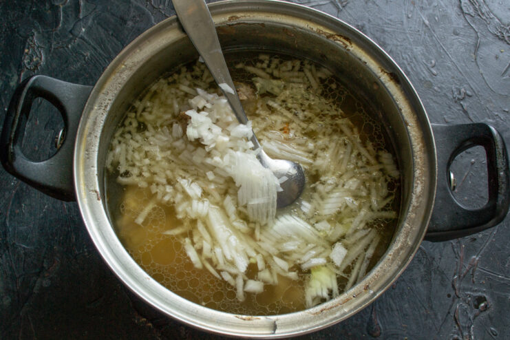 Chopped onions being added to the pot with cooked ribs and broth.