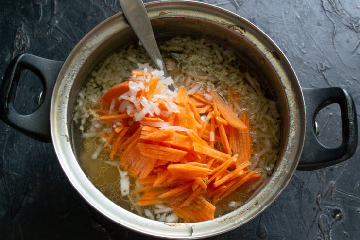 Thinly julienned carrots on a cutting board, ready to be added to the soup.