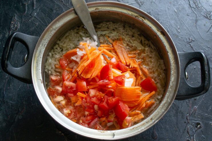 Diced tomatoes being added from a cutting board into the pot of borscht.