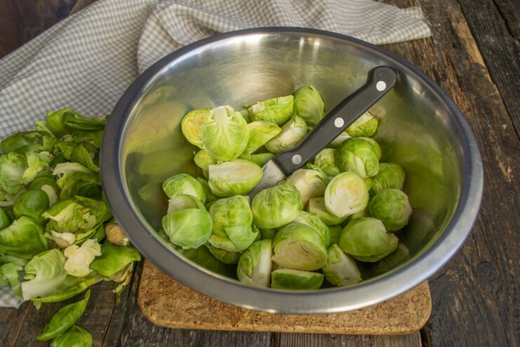 Trimming and halving fresh Brussels sprouts before cooking. Fresh Brussels sprouts being trimmed and cut in half on a cutting board.