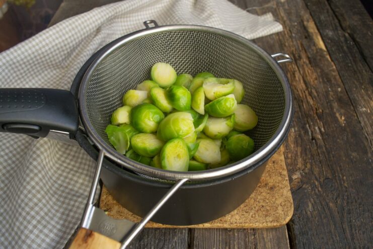 Draining the boiled Brussels sprouts to remove excess water. Boiled Brussels sprouts being drained in a metal colander.
