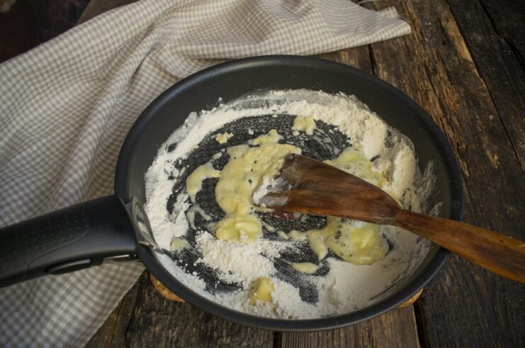 Combining butter and toasted flour to create the roux base for the cream sauce. Melting butter into toasted flour in a skillet to make a roux.