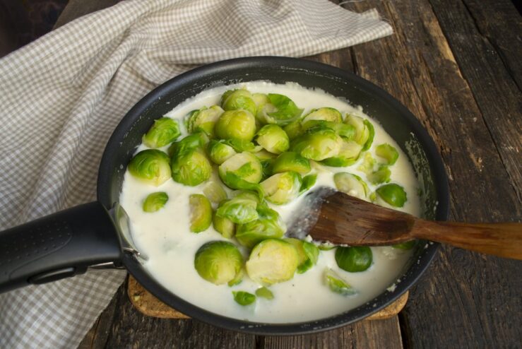 Coating the boiled Brussels sprouts evenly with the creamy sauce. Cooked Brussels sprouts being mixed into the creamy sauce in a skillet.