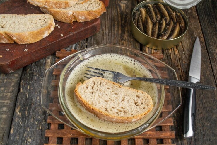 Dipping the Bread Slice into the Egg Mixture A slice of dark bread being dipped into a bowl of whisked egg.