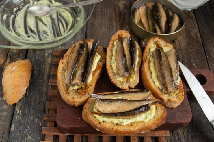 Arranging the Smoked Sprats on Top Smoked sprats being carefully arranged on top of the cheese spread on a sandwich.