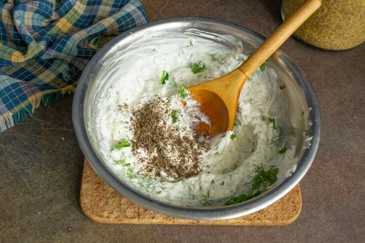 Finishing the creamy sauce for the bulgur and pumpkin dish Whisking water and spices into the smetana and herb mixture to create a sauce.